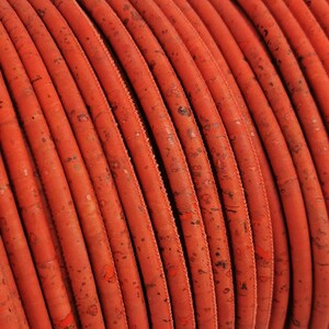 May include: Close-up of a spool of orange cork cord. The cord is made of natural cork and has a slightly textured surface.