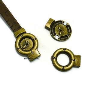 May include: Three gold-toned metal watch strap connectors. One connector has a clock face with hands, another has a circular opening, and the third is a flat piece with a clock face.