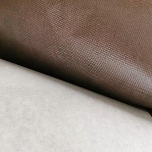 May include: Close-up of a brown textured fabric roll. The fabric has a subtle sheen and a slightly rough texture.