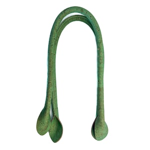 Puede incluir: Un asa de bolso verde en forma de U hecha de material texturizado. El asa tiene un diseño curvo con extremos redondeados y una división en la base. El asa está sobre un fondo blanco.