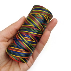 May include: A spool of colorful waxed thread, featuring a variety of colors including red, yellow, green, blue, and black. The thread is wound tightly around the spool, creating a visually appealing pattern.