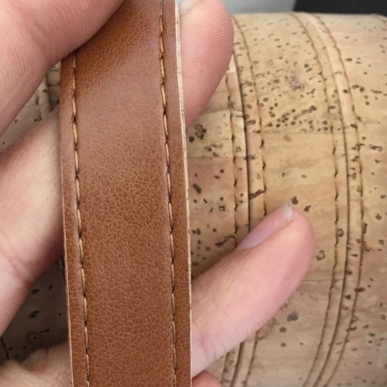 May include: Close-up of a brown leather strap with stitching. The strap is next to a cork surface.