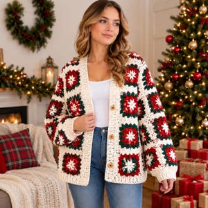 Könnte beinhalten: Eine langärmelige Häkelstrickjacke mit Granny-Square-Muster in Creme, Rot und Dunkelgrün. Das Kleidungsstück hat einen V-Ausschnitt, eine cremefarbene gerippte Kante entlang der Vorderseite und drei runde Holzknöpfe als Verschluss.