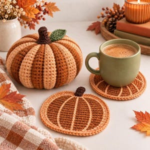 May include: A crocheted pumpkin with alternating light and dark orange vertical segments, a dark brown stem, and a green leaf. Two matching circular crocheted pumpkin coasters are included, one holding a light green ceramic mug of coffee.