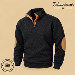 May include: A dark charcoal gray long-sleeve pullover sweater featuring a stand-up collar with a tan button-down placket and matching tan elbow patches on each sleeve. The sweater has a textured knit fabric and ribbed cuffs and hem.