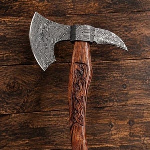 May include: A hand axe featuring a patterned Damascus steel head with a wide, curved blade and a pointed rear spike. The handle is crafted from dark brown wood and displays an intricate, carved braided pattern along the center grip area.