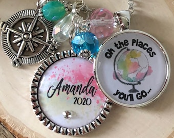 May include: A silver necklace with a compass charm, a charm with the text "Oh the Places You'll Go..." and a charm with the text "Amanda 2020". The charms are surrounded by colorful beads.