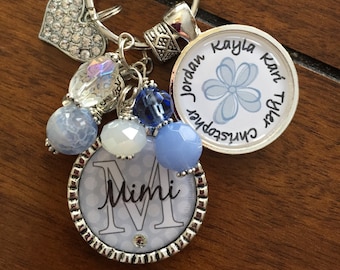 May include: A silver keychain with a blue and white charm that says "Christopher Jordan Tyler Kayla Kari" and a silver charm with a blue and white polka dot background and the letter "M" with the word "Mimi" underneath.
