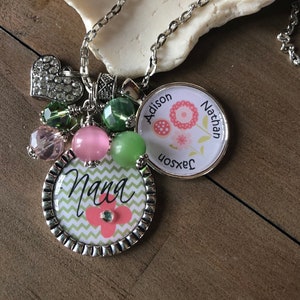 May include: A silver necklace with a charm that says "Nana" and a charm with a floral design and the names "Addison", "Nathan", and "Jackson". The necklace also has several pink and green beads.