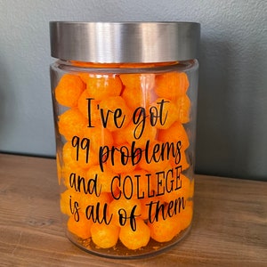 May include: A glass jar with a silver lid filled with orange cheese puffs. The jar has a black vinyl sticker with the text "I've got 99 problems and COLLEGE is all of them."