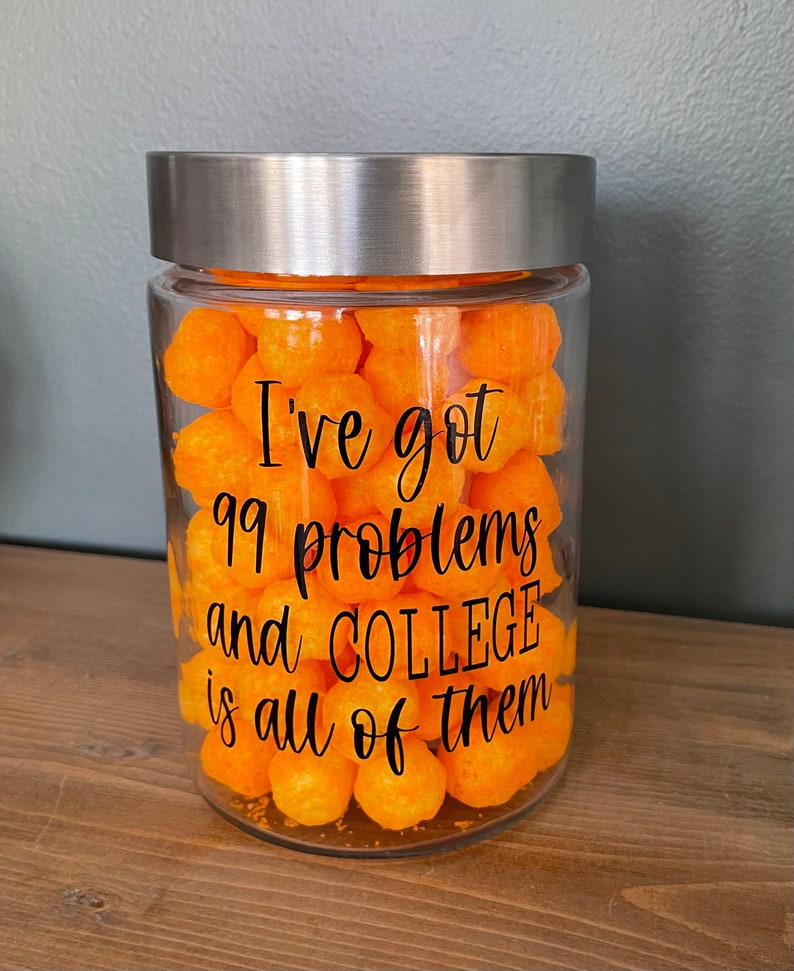 May include: A glass jar with a silver lid filled with orange cheese puffs. The jar has a black vinyl sticker with the text "I've got 99 problems and COLLEGE is all of them."