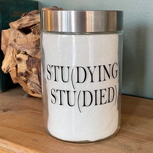 May include: A clear glass jar with a silver lid and a white paper towel inside. The jar has a black vinyl sticker with the text "STU(DYING) STU(DIED)"