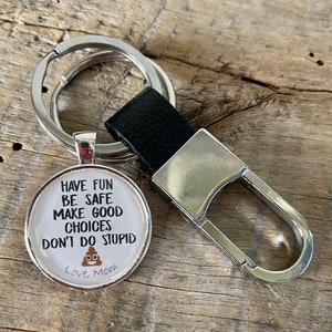May include: A silver keychain with a round charm that says "Have fun be safe make good choices don't do stupid" with a poop emoji and "Love, Mom".