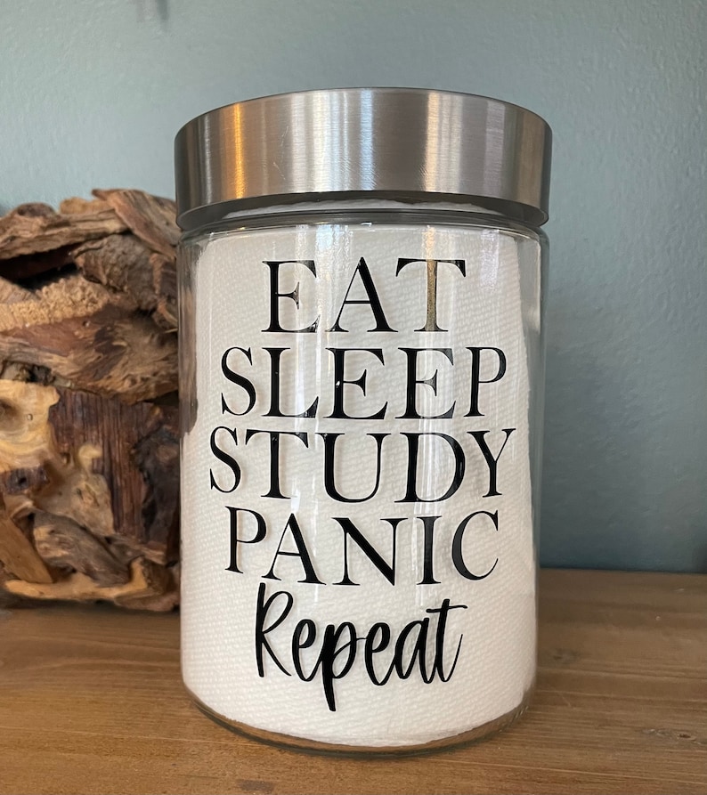 May include: A clear glass jar with a silver lid and a white label that reads "Eat Sleep Study Panic Repeat".