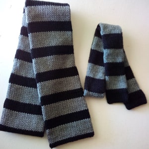 May include: Two striped scarves, one long and one short, in black and gray. The scarves are made of a soft, knitted fabric.