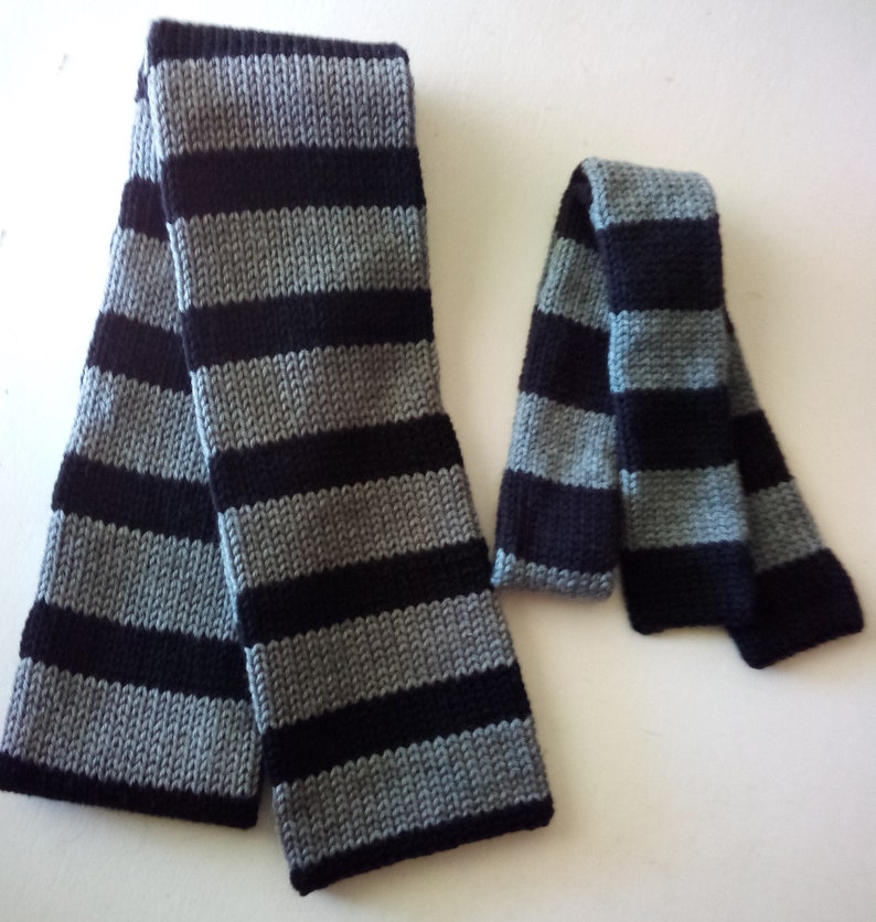 May include: Two striped scarves, one long and one short, in black and gray. The scarves are made of a soft, knitted fabric.