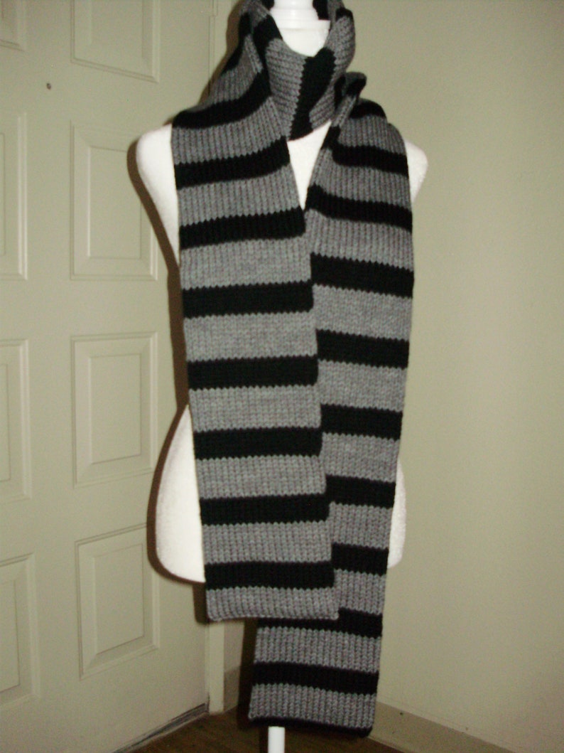 May include: A gray and black striped knit scarf. The scarf is folded in half and draped over a mannequin.