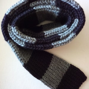 May include: A black and gray striped knitted scarf. The scarf is rolled up and the ends are visible.