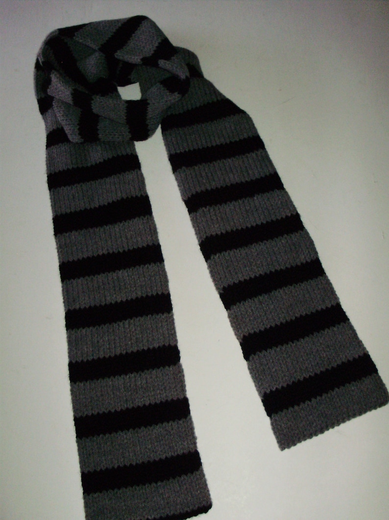 May include: A gray and black striped knitted scarf. The scarf is folded in half and the ends are hanging down.