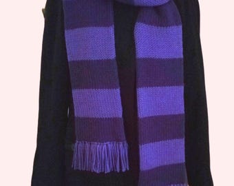 May include: A purple and dark purple striped knitted scarf with fringe on the ends. The scarf is draped around a mannequin wearing a black coat.