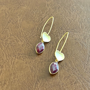 May include: A pair of gold earrings with a heart-shaped charm and a red gemstone dangle.