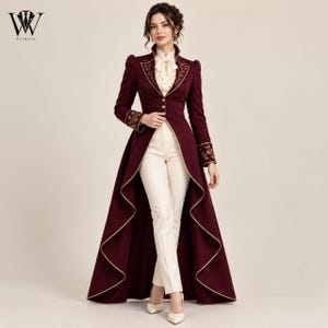 May include: A burgundy long-tailed coat with gold piping and floral embroidery on the lapels and cuffs, worn over a cream-colored ruffled blouse and slim-fit cream trousers. The coat features a high collar and a button-down front closure.