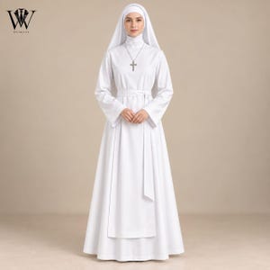 May include: A floor-length white habit featuring long sleeves, a high neckline, and a matching waist tie. The garment includes a white head covering and a silver-toned cross pendant necklace. The design is solid white with a clean, structured silhouette.