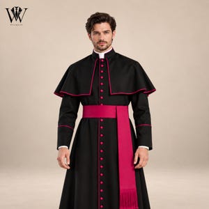 May include: A black cassock featuring a vibrant magenta sash with fringe, a matching magenta-trimmed capelet, and a row of magenta buttons running down the front. The garment includes a high collar with a white clerical tab insert at the neckline.