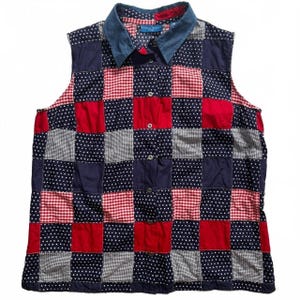 Op de afbeelding: Een mouwloos overhemd met knoopsluiting en een patchworkontwerp van rode, witte en marineblauwe vierkanten. Het patroon wisselt af tussen effen rood, marineblauw met witte stippen en rood-witte vichy-ruitjes. Het heeft een spijkerstofkleurige kraag.