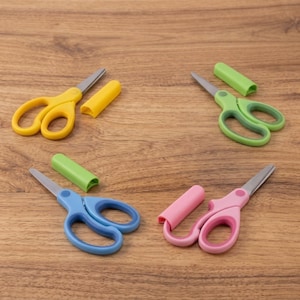 May include: Four pairs of scissors with metal blades and plastic handles in yellow, green, blue, and pink. Each pair of scissors includes a matching plastic protective cap for the blade, arranged in a scattered layout on a wooden surface.