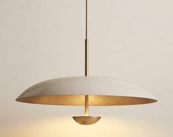Puede incluir: Una lámpara colgante con una pantalla en forma de cúpula ancha, poco profunda y de color blanco roto mate, suspendida por una fina varilla de latón. Un componente de latón más pequeño en forma de cuenco refleja la luz hacia la cúpula.