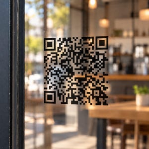 May include: A black QR code sticker applied to a transparent glass surface. The square code features a complex pattern of black pixels and three distinct square alignment markers in the corners, designed for digital scanning and information access.