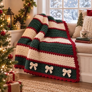 May include: A crocheted throw blanket featuring horizontal stripes in dark green, cream, and thin red lines. The blanket has a scalloped red border and is decorated with three cream-colored crocheted bows along the bottom edge of the fabric.