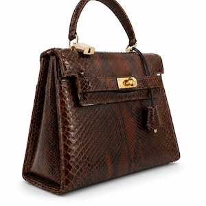 May include: A structured handbag featuring a dark brown snakeskin-patterned exterior. The bag includes a single top handle, a gold-toned metal turn-lock closure on the front flap, and a small gold-toned padlock attached to the handle base.