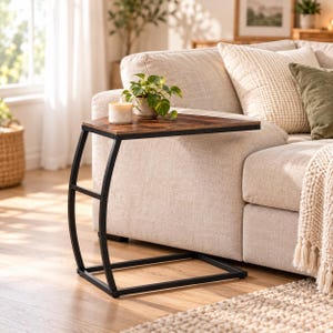 Puede incluir: Una mesa auxiliar en forma de C con un tablero de acabado en madera marrón oscuro y una estructura de metal negro. La mesa cuenta con un soporte curvo y una base rectangular, ofreciendo una superficie para una planta y una vela.