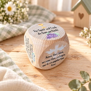 Könnte beinhalten: Ein Holzwürfel mit abgerundeten Kanten, bedruckt mit deutschem Text und Illustrationen. Die Oberseite zeigt einen Kelch und Weintrauben mit dem Text "Für Speis und Trank dir Gott sei Dank!". Die Seite zeigt eine weiße Taube und das Gebet "Komm, Herr Jesus".