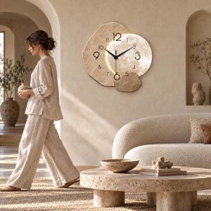 May include: A wall clock featuring a textured, irregular beige frame and a circular, illuminated moon-like face. The clock has black hour and minute hands, with black numerals 3, 6, 9, and 12, and smaller markers for the remaining hours.