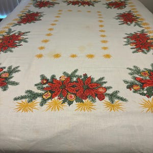 May include: White tablecloth with a Christmas theme featuring red poinsettia flowers, green pine branches, and gold stars.