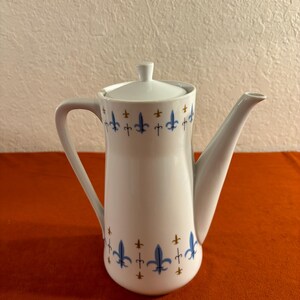 May include: White ceramic coffee pot with a blue and gold fleur-de-lis design.