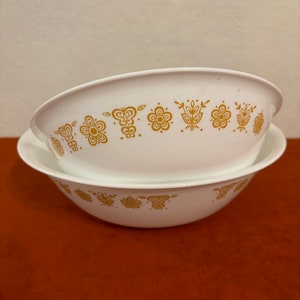 May include: Two white ceramic bowls with a gold floral pattern. The bowls are stacked on top of each other.