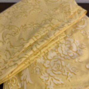 May include: A stack of yellow fabric with a white floral pattern. The fabric is folded in thirds and has a soft, textured surface.