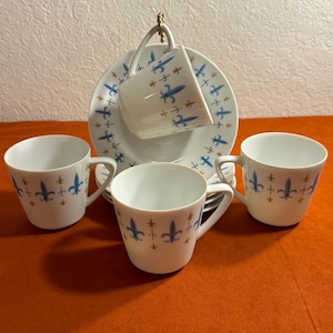 May include: Set of four white porcelain teacups and saucers with a blue and gold fleur-de-lis pattern.