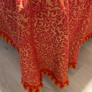 May include: Red and yellow tablecloth with a floral pattern and fringe trim.