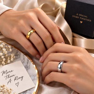 Puede incluir: Un anillo de banda en tono dorado pulido y un anillo de banda en tono plateado pulido. La caja de regalo negra presenta el texto A SPECIAL STORY TOGETHER con un icono de corazón. Una tarjeta blanca muestra el texto More Than A Ring con un corazón.