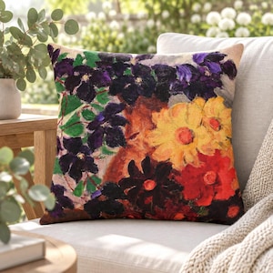 以下が含まれることがあります： 鮮やかで絵画的な花柄がプリントされた正方形のクッション。深みのある紫、鮮やかな黄色、大胆な赤の花々が、質感のあるアースブラウンの背景に描かれており、全体に緑の葉のアクセントが散りばめられたデザインです。