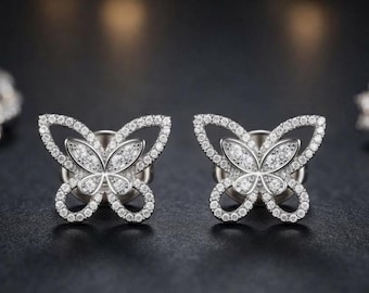 May include: A pair of silver-toned stud earrings shaped like butterflies. Each earring features a central butterfly motif filled with small, clear, sparkling stones, surrounded by a delicate, open-work frame encrusted with tiny, shimmering white crystals.
