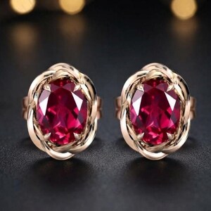 Peut inclure: Une paire de boucles d'oreilles avec de grandes pierres pr&eacute;cieuses ovales rouge fonc&eacute; serties dans une monture en m&eacute;tal dor&eacute; torsad&eacute; et poli. Le design pr&eacute;sente une pierre centrale &agrave; facettes entour&eacute;e d'un bord m&eacute;tallique entrelac&eacute;.