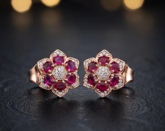 Peut inclure: Une paire de boucles d'oreilles à clous en or rose en forme de fleurs. Chaque boucle présente six rubis rouge foncé taille ovale disposés en pétales autour d'un centre de petits diamants blancs ronds, avec des diamants sertis sur les bords.