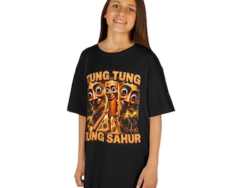 May include: A black short-sleeved t-shirt featuring a graphic print of a central brown character holding a wooden bat, flanked by two large faces. The text TUNG TUNG TUNG SAHUR is printed in orange block letters above and below the central figure.
