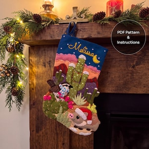 May include: A blue felt Christmas stocking featuring an embroidered desert landscape with cacti, a bird wearing a scarf, and a javelina wearing a Santa hat. The name Melissa is stitched in yellow thread at the top. Includes PDF Pattern & Instructions.
